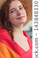 Vertical video. Portrait of young woman in a hat with long red hair covering herself in lgbt flag while looking at camera. 143848330