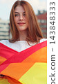 Vertical video. Portrait of a young woman with long red hair covering herself in lgbt flag while looking to camera. 143848333