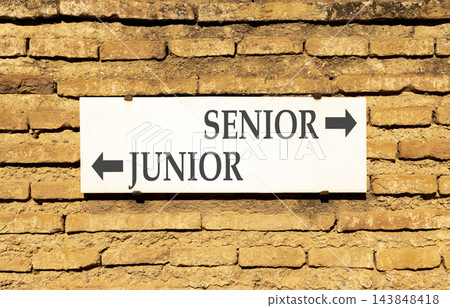 Senior or junior words symbol. Concept words Senior Junior on beautiful white sign plate. Beautiful brick wall background. Business and senior or junior concept. Copy space. 143848418
