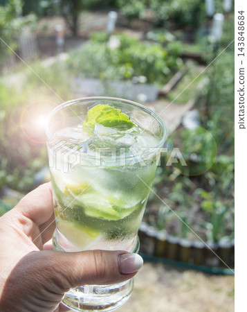 A refreshing mojito drink in a woman's hand. Vertical, outdoors, on a sunny summer day A refreshing mojito drink in a woman's hand. Vertical, outdoors, on a sunny summer day 143848684
