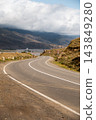 Winding mountain road through rocky hills under cloudy sky 143849280