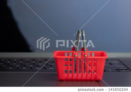 Red plastic shopping basket on laptop background Red plastic shopping basket on laptop background 143850204