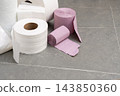 Assorted White and Purple Toilet Paper Rolls and Paper Towels on a Grey Bathroom 143850360
