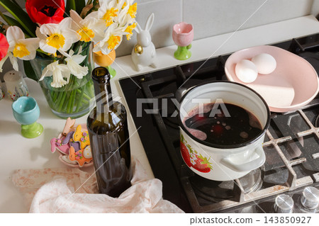 A pot, red wine, and a bowl of eggs sit on a stove in a home kitchen, ready for dyeing eggs as part of an Easter holiday activity A pot, red wine, and a bowl of eggs sit on a stove in a home kitchen, ready for dyeing eggs as part of an Easter holiday activity 143850927