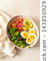 Bowls of beet hummus contain chickpeas, boiled eggs, fresh broccoli, and microgreens salad. Glasses of water with lemon slices add freshness to the table 143850929