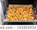 Eggplant, zucchini, carrots, onions, garlic, cauliflower, and peppers bake on a tray in an oven during meal preparation at home 143850934