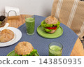 At breakfast, homemade burgers with lettuce and tomato sit on green plates on a wooden table, with green drinks beside them in a dining area 143850935