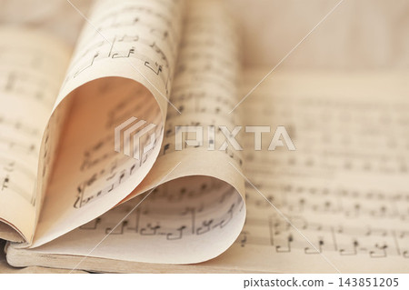 Heart shaped page fold in vintage sheet music book. Close-up selective focus photograph of vintage sheet music book pages folded into heart shape, symbolizing love for music, romantic melody Heart shaped page fold in vintage sheet music book. Close-up selective focus photograph of vintage sheet music book pages folded into heart shape, symbolizing love for music, romantic melody 143851205
