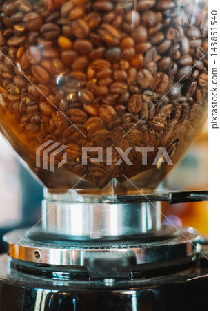 Close up of roasted coffee beans inside a professional coffee grinder, showing detailed bean texture and metal equipment during coffee preparation. 143851540