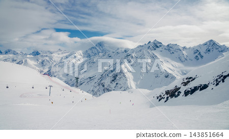 Snowy ski slope with distant skiers and chairlift beneath Mount Elbrus and Caucasus peaks 143851664