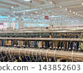 Clothing racks with hangers in retail store, blurred background. Close-up view of metal clothing rails filled with clothes hangers, large brightly lit fashion shop with bokeh bokeh light background 143852603
