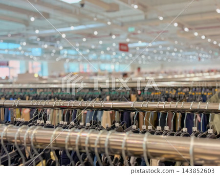 Clothing racks with hangers in retail store, blurred background. Close-up view of metal clothing rails filled with clothes hangers, large brightly lit fashion shop with bokeh bokeh light background Clothing racks with hangers in retail store, blurred background. Close-up view of metal clothing rails filled with clothes hangers, large brightly lit fashion shop with bokeh bokeh light background 143852603