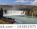 Godafoss waterfall and swirling river beneath snow-streaked hills in North Iceland 143852975