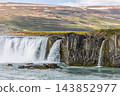 Powerful Godafoss waterfall beside basalt cliffs and snow-streaked Icelandic hills 143852977