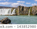 Godafoss waterfall over turquoise waters framed by rugged cliffs in North Iceland 143852980