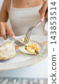 Woman cutting a boiled egg beside bread on a floral plate 143853514