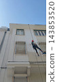 Rope-access worker suspended beside a white building facade 143853520
