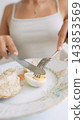 Woman cutting a boiled egg with a knife and fork at breakfast 143853569