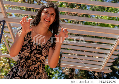 Playful woman smiling and making claw gestures beneath a garden pergola Playful woman smiling and making claw gestures beneath a garden pergola 143853920