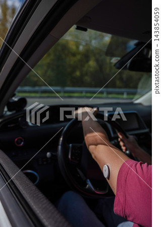 A woman driving a car with a continuous glucose monitoring sensor. A woman driving a car with a continuous glucose monitoring sensor. 143854059