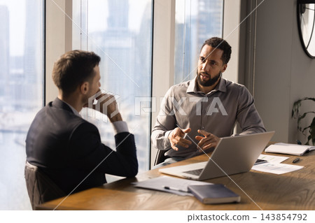 Two multiethnic businessmen discussing strategy during meeting at office Two multiethnic businessmen discussing strategy during meeting at office 143854792