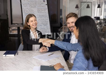 Businesswoman shaking hands with corporate clients making agreement at table Businesswoman shaking hands with corporate clients making agreement at table 143854909