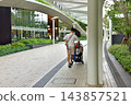 A father pushing a stroller in the new pedestrian walkway at Hamamatsucho Station, looking up at the monorail. 143857521