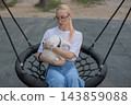 A woman is swinging on a swing while out for a walk with her cat. 143859088