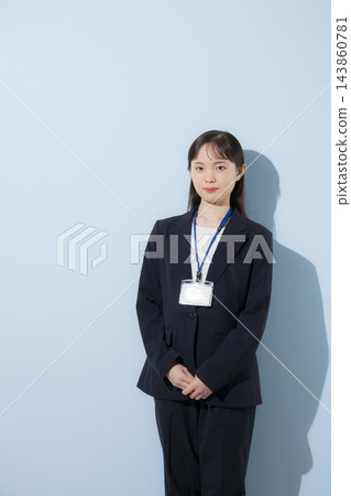 [淺藍色背景] 一位二十出頭的年輕日本女性，身穿西裝，脖子上掛著員工證，神情嚴肅認真地站著。 143860781