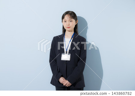 [淺藍色背景] 一位二十出頭的年輕日本女性，身穿西裝，脖子上掛著員工證，神情嚴肅認真地站著。 143860782