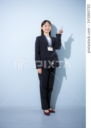 [淺藍色背景] 一位二十出頭的年輕日本女子，身穿西裝，脖子上掛著員工證，正在指著什麼。 143860785