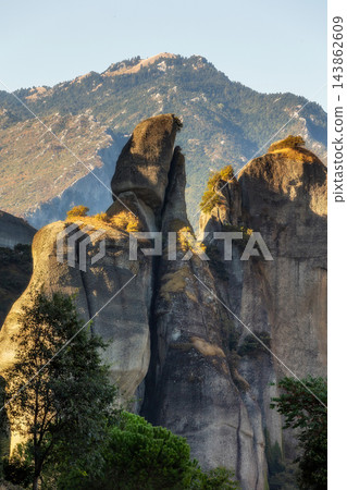 Meteora Greece massive rock pillars glowing in sunset light behind green trees Meteora Greece massive rock pillars glowing in sunset light behind green trees 143862609