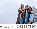 Mother, father and teenage daughter sitting on a stone by the sea, looking into the distance in a thoughtful mood. Concept of a family thinking about the future and making a decision together. 143867595