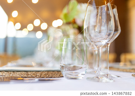 Elegant restaurant table setting with wine glasses and warm bokeh lights Elegant restaurant table setting with wine glasses and warm bokeh lights 143867882