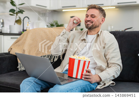 Young man watches comedy on laptop eats popcorn laughs out loud cheerful reaction happy movie time 143869451