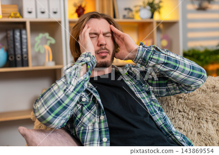 Young man on home sofa rubbing temples with closed eyes showing burnout fatigue after work indoors Young man on home sofa rubbing temples with closed eyes showing burnout fatigue after work indoors 143869554