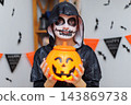 Child in skeleton costume holding pumpkin bucket at Halloween party 143869738