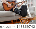 Person with leg injury playing guitar on sofa at home 143869742