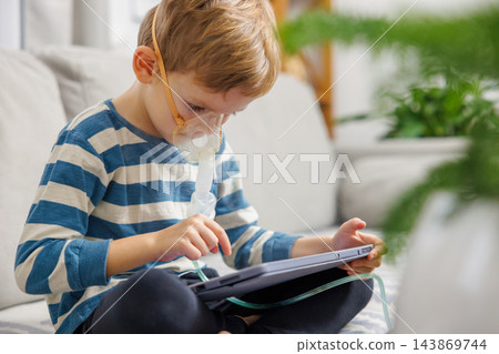 Child using nebulizer and tablet on sofa Child using nebulizer and tablet on sofa 143869744