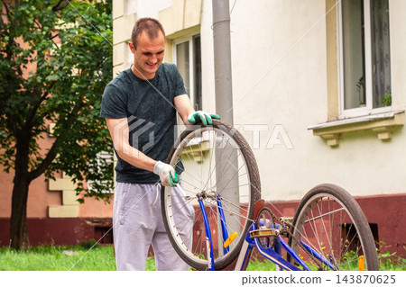 Man examining bike chain and gears for wear. Upside down position reveals issues. Practical competence outside house Man examining bike chain and gears for wear. Upside down position reveals issues. Practical competence outside house 143870625