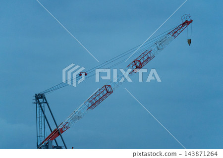 大型建築起重機的主體結構和紅白相間的鋼製吊臂斜伸向蔚藍的夜空。 143871264