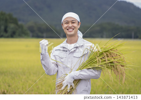 一位四十多歲、微笑的稻農,手裡拿著一捆稻稈。 一位四十多歲、微笑的稻農,手裡拿著一捆稻稈。 143871413
