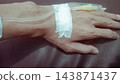 Hand rests gently on dark surface. Medical IV line secures wrist with tape. Calm posture suggests patient comfort. Ideal for healthcare, medical education, or wellness contexts 143871437