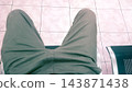 Person sits relaxed on metal bench. Green pants rest neatly on tiled floor. Pink tiles form patterned background. Metal chair edges reflect soft light. Patiently waiting, still, calm posture 143871438