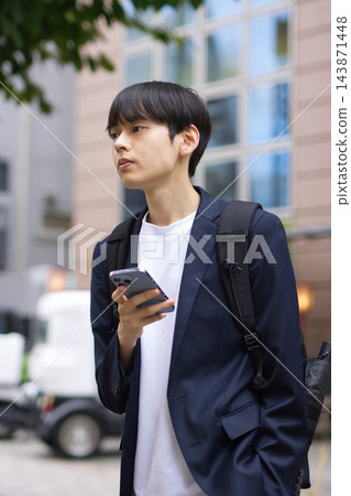一名二十多歲的男子在街上拿著智慧型手機。 一名二十多歲的男子在街上拿著智慧型手機。 143871448