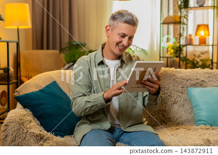 Middle-aged man on home sofa holds framed old photo smiles softly and recalls warm family memories Middle-aged man on home sofa holds framed old photo smiles softly and recalls warm family memories 143872911