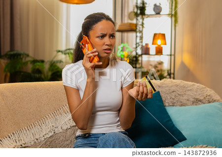 African American young woman on home sofa calling bank support to explain bank card payment problem 143872936
