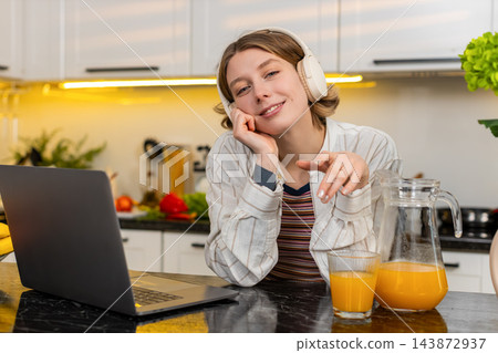 Young woman enjoying music in headphones by laptop during a healthy breakfast break in home kitchen 143872937