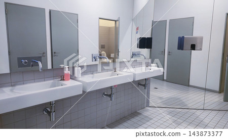 Clean public restroom with multiple sinks, mirrors and toilet cubicles in a modern facility. Concepts: public hygiene, sanitation infrastructure, commercial interiors, facility maintenance Clean public restroom with multiple sinks, mirrors and toilet cubicles in a modern facility. Concepts: public hygiene, sanitation infrastructure, commercial interiors, facility maintenance 143873377