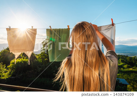 Woman Hanging Laundry Outdoors in Sunlit Mountain Landscape 143874109